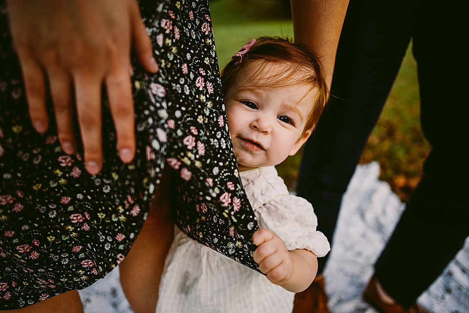 Baby girl peeking out from behind mom's dress
